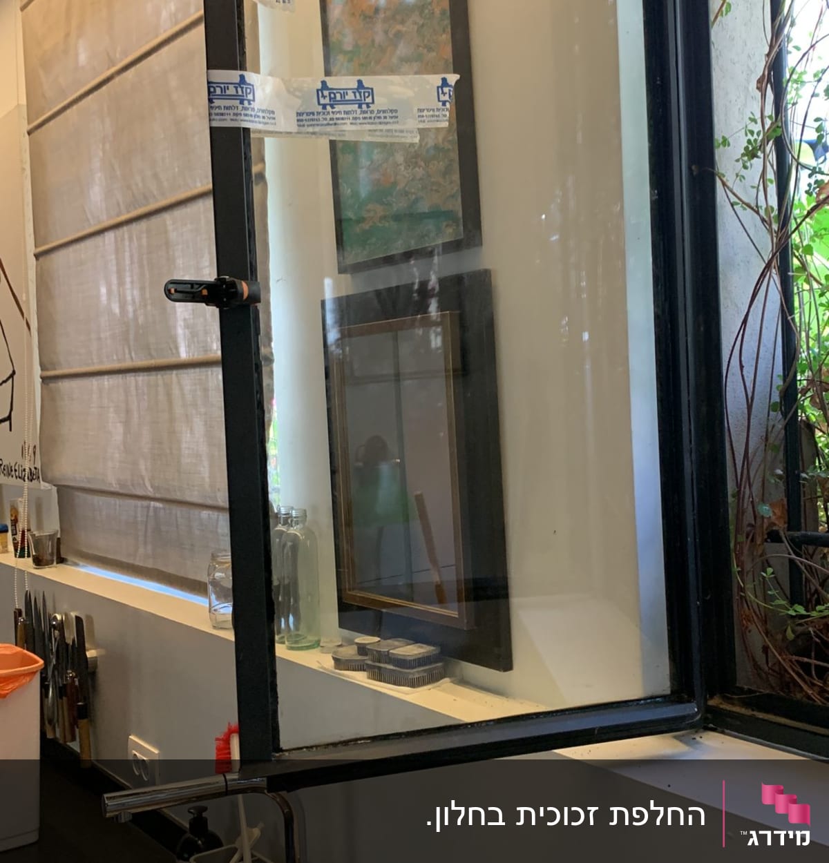 חלון זכוכית פתוח עם מסגרת שחורה וסרטי הדבקה